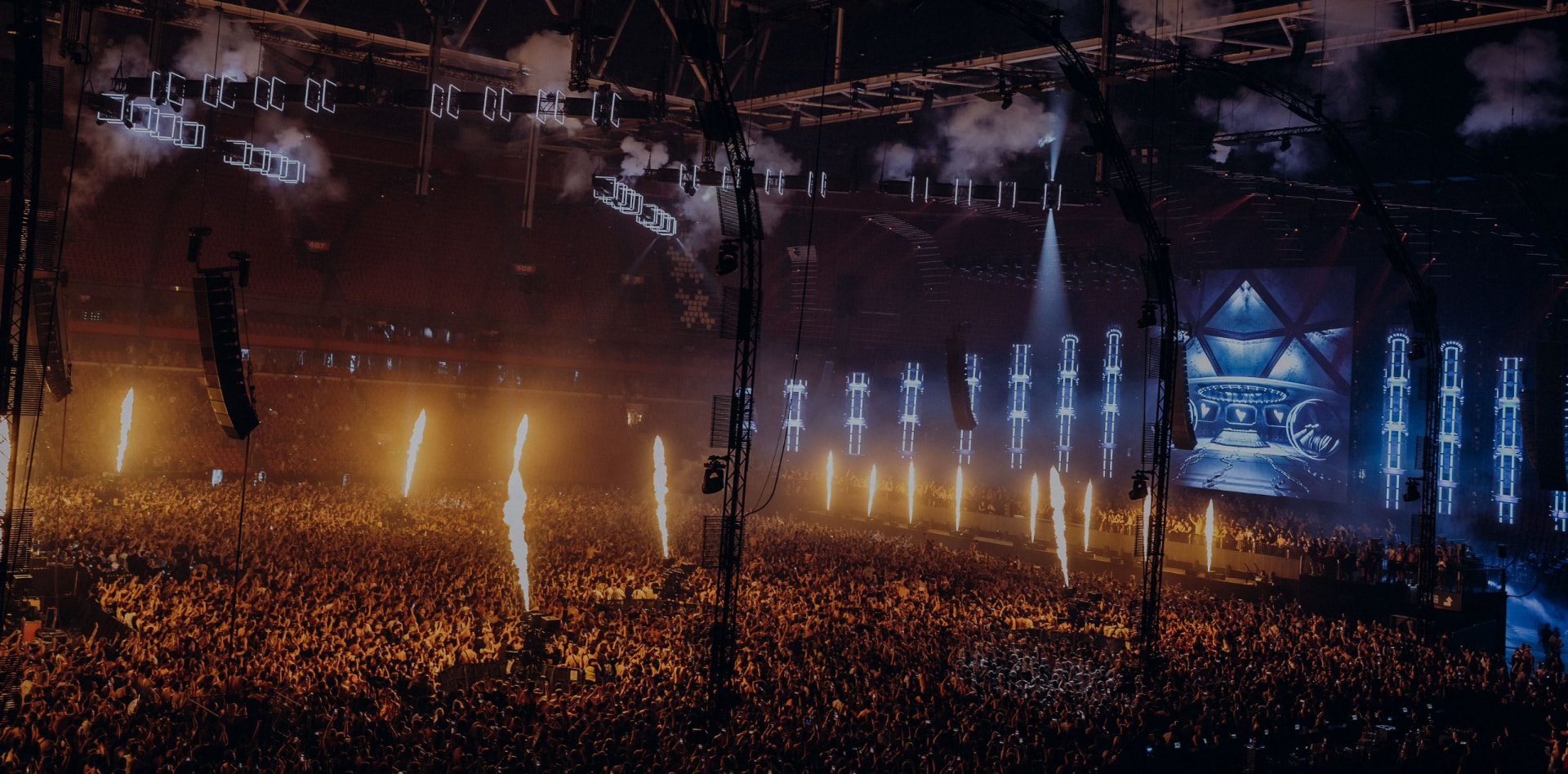 Packed crowd facing a lit stage with pyrotechnics at Verknipt